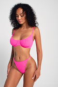 A model wearing a bright pink neon bra and matching thong with adjustable straps, showcasing a soft mesh fabric.