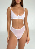 A woman wearing a white lingerie set which includes a bra and high thong.